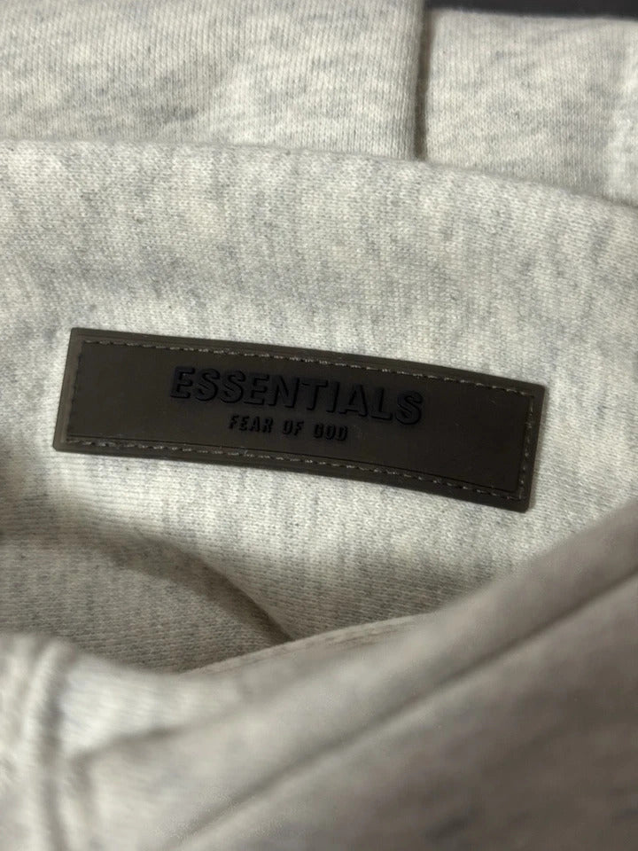 Gray fabric with a black leather label reading 'ESSENTIALS' and 'FEAR OF GOD'.