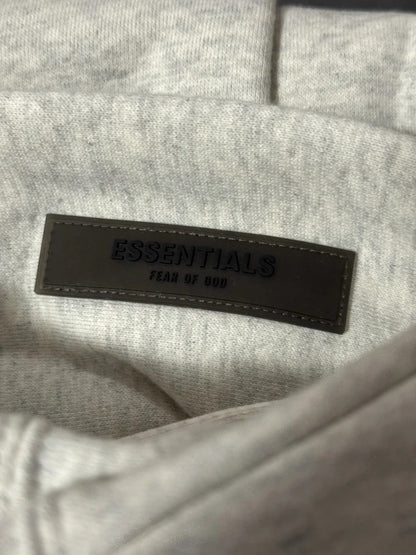 Gray fabric with a black leather label reading 'ESSENTIALS' and 'FEAR OF GOD'.