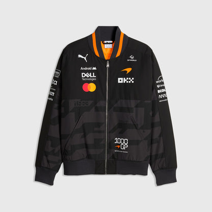 Front view of the black and gray McLaren inspired 1000th GP unisex bomber jacket with multi-sponsor logos, orange striped collar, and 1000 GP badge by TassFit Performance.